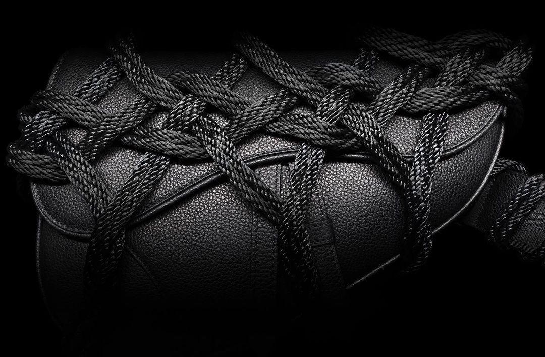 Close-up shot of a black leather handbag wrapped with black rope, presented against a stark black background for a high-contrast, fashionable look.