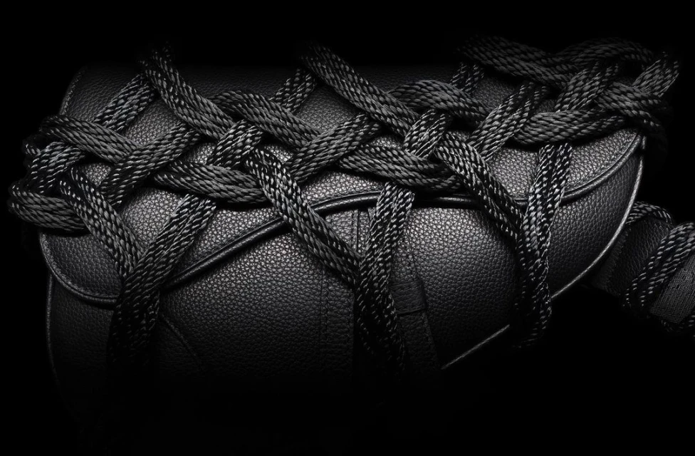Close-up shot of a black leather handbag wrapped with black rope, presented against a stark black background for a high-contrast, fashionable look.
