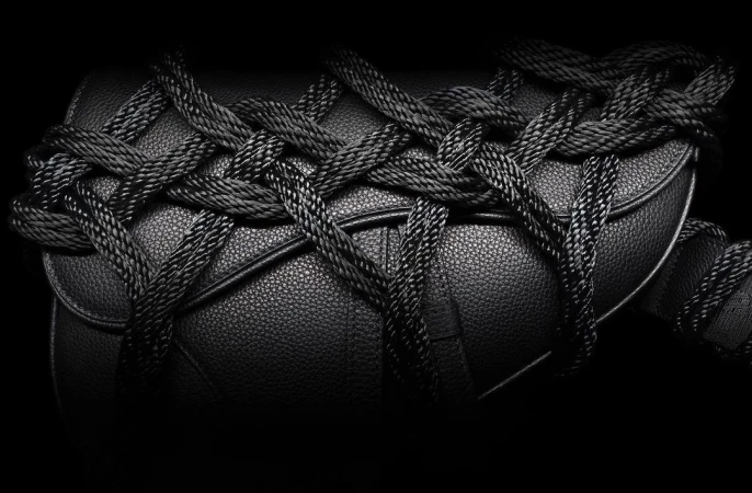 Close-up shot of a black leather handbag wrapped with black rope, presented against a stark black background for a high-contrast, fashionable look.