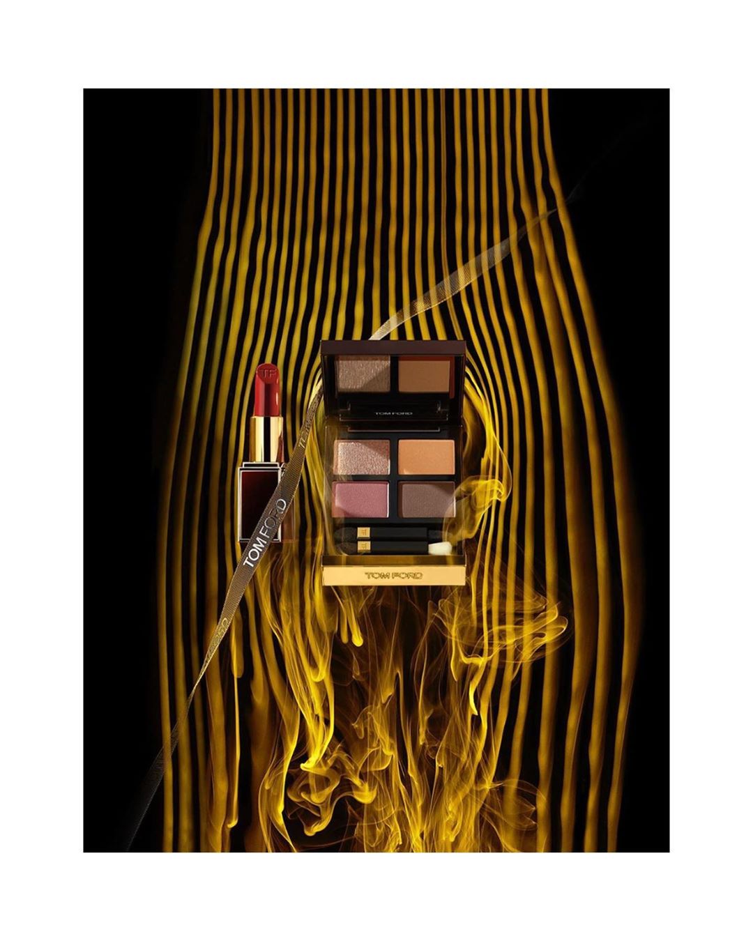 Tom Ford brand makeup featuring red lipstick and eyeshadow palette on a black backdrop with gold, wave-like accents. 