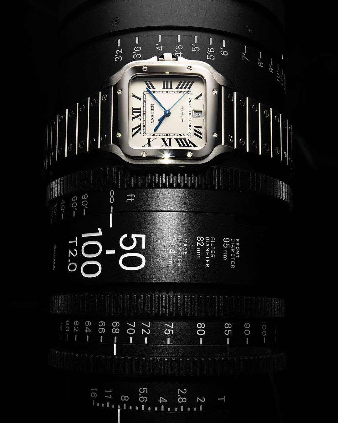 Luxury silver Cartier Santos wristwatch on a camera lens, studio shot. High-end timekeeping, focus on precision watchmaking craftsmanship.