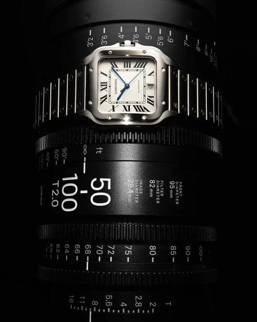 Luxury silver Cartier Santos wristwatch on a camera lens, studio shot. High-end timekeeping, focus on precision watchmaking craftsmanship.