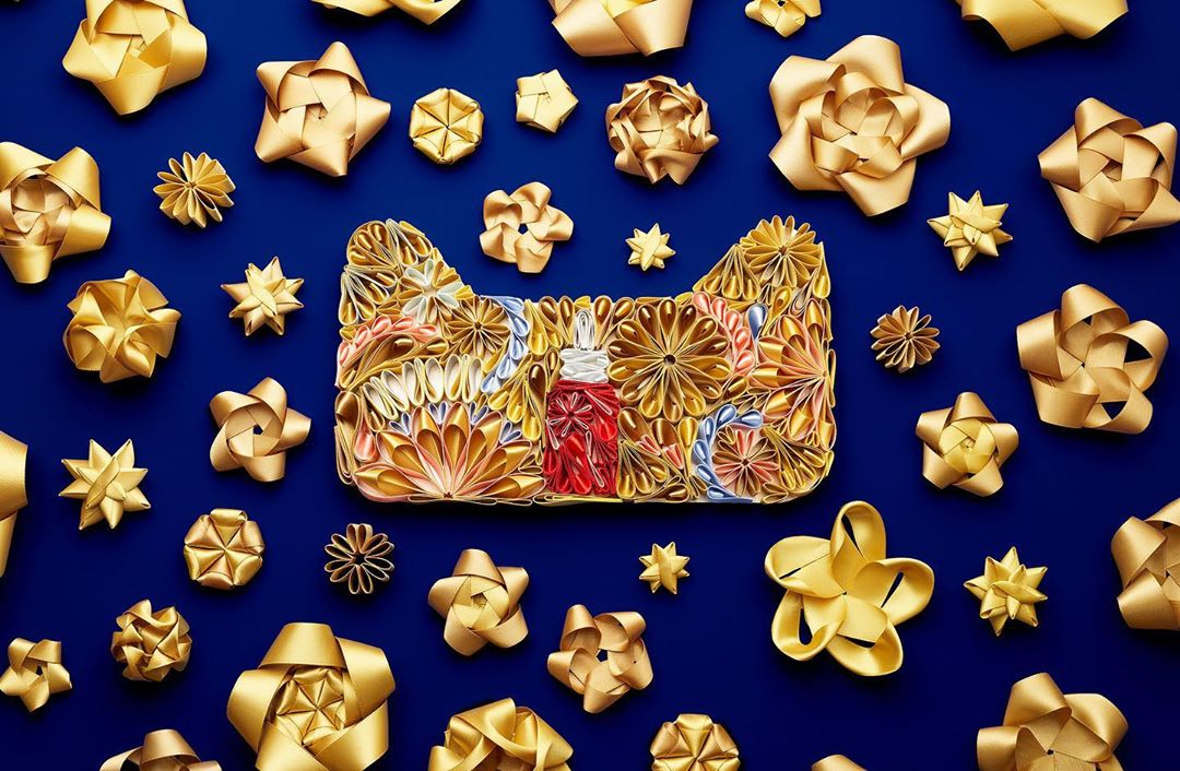 Flat lay of cat silhouette filled with ribbon flowers, small starbursts, and a perfume bottle on a dark blue background.