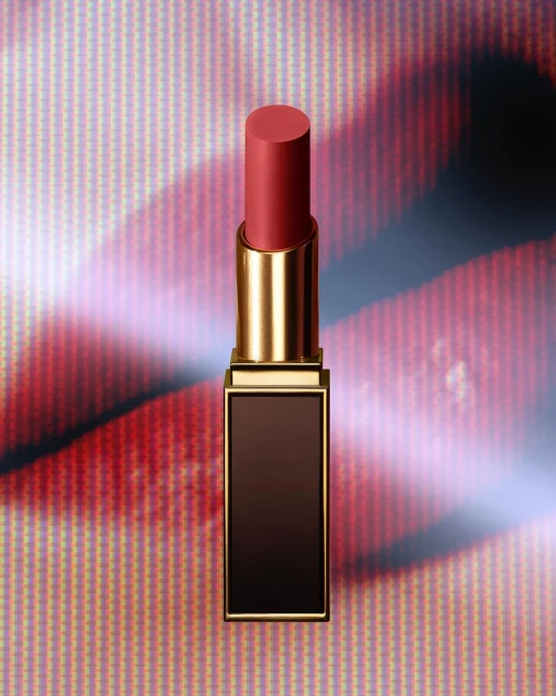 Close-up of a coral lipstick tube with a gold case, placed in front of a pink and red patterned background for beauty advertising.