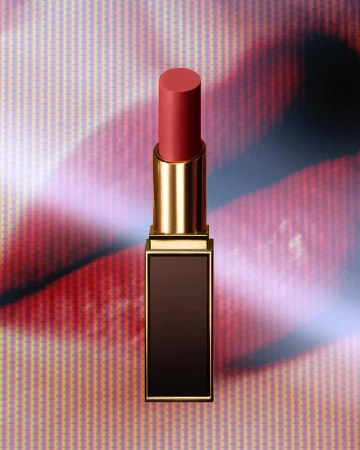 Close-up of a coral lipstick tube with a gold case, placed in front of a pink and red patterned background for beauty advertising.