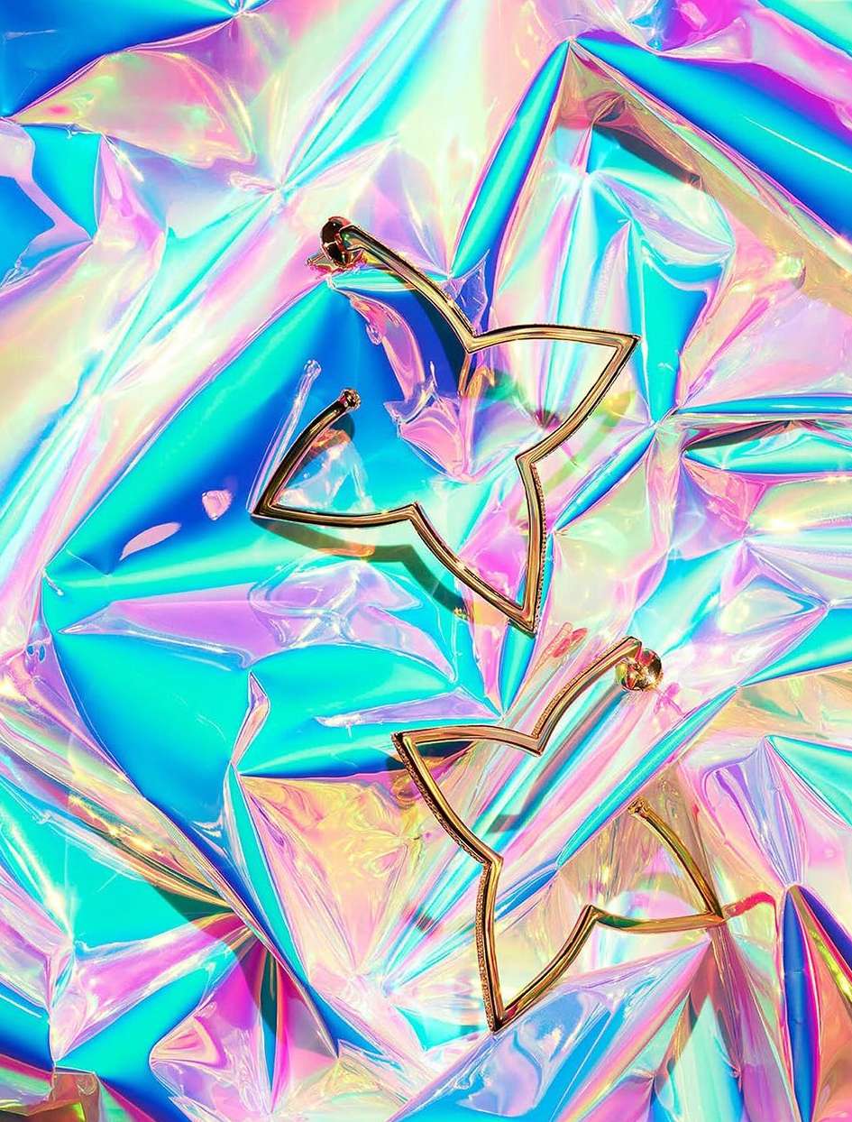 Close-up of gold star earrings on iridescent cellophane. Flat lay showcasing fashion earrings with bright, shiny background.