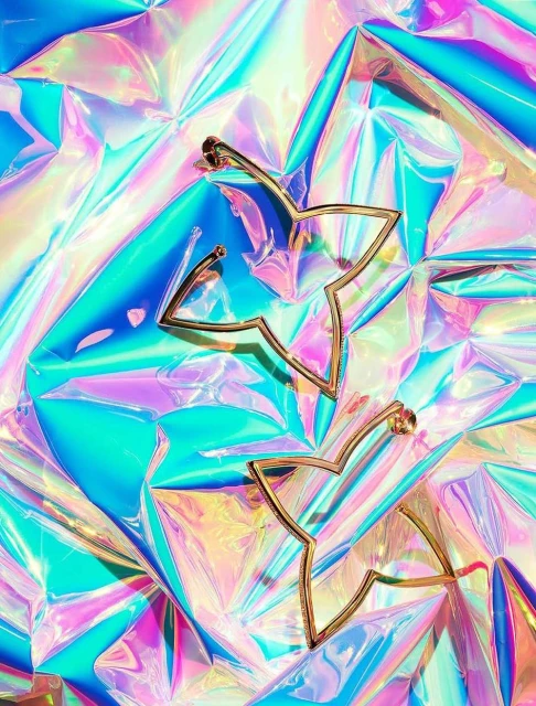 Close-up of gold star earrings on iridescent cellophane. Flat lay showcasing fashion earrings with bright, shiny background.