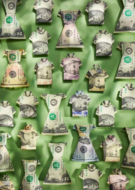 Arrangement of folded US dollar bills shaped as dresses and shirts on a green background. Creative money and finance concept.