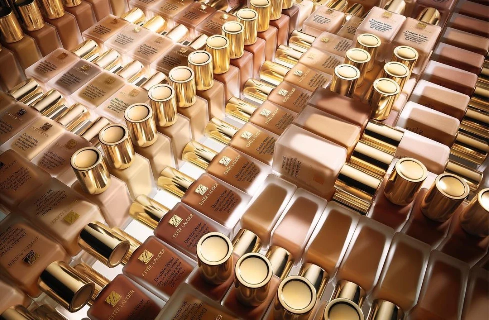High-angle, overhead shot of many bottles of Estée Lauder Double Wear foundation in various shades, neatly arranged on a surface.