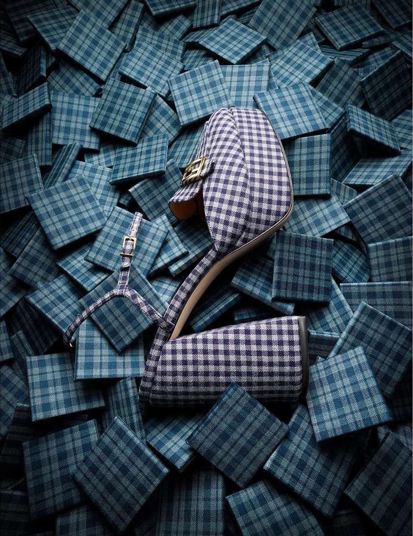 Close-up of a plaid-patterned high-heeled shoe surrounded by plaid squares on a patterned studio backdrop for fashion marketing.