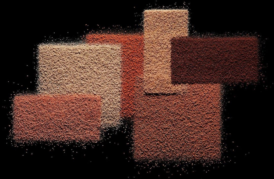 Arrangement of rectangular areas covered with tan, brown, and terracotta powder against a stark black backdrop, studio shot.