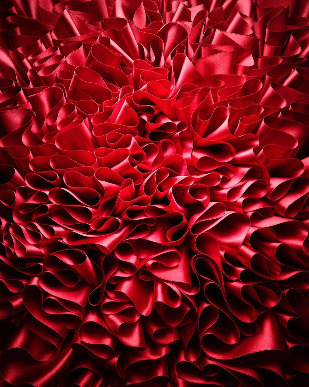 Close-up of layered, ruffled red silk ribbon creates a luxurious abstract texture, with dark shadows and dramatic lighting.