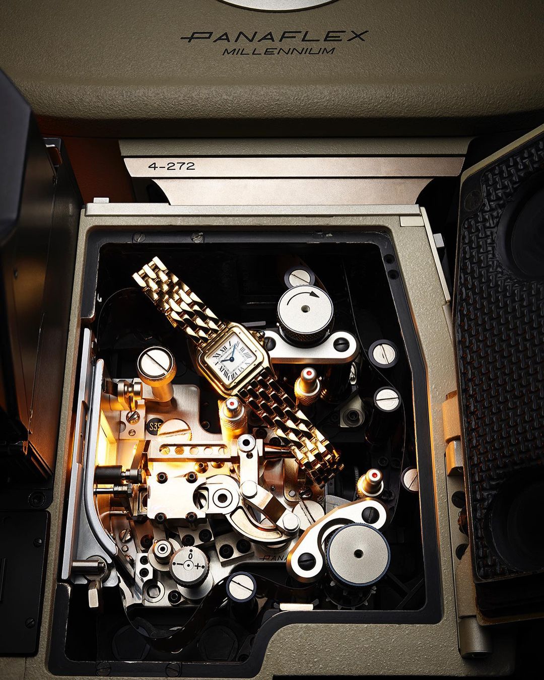 Gold wristwatch on the inside of a film camera mechanism, highlighting intricate gears and internal components in warm, directional lighting.