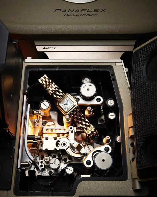 Gold wristwatch on the inside of a film camera mechanism, highlighting intricate gears and internal components in warm, directional lighting.