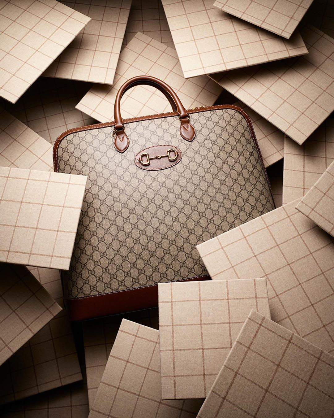Gucci bag surrounded by square tiles featuring a beige and brown plaid pattern. The bag is tan with a monogram print and brown trim.