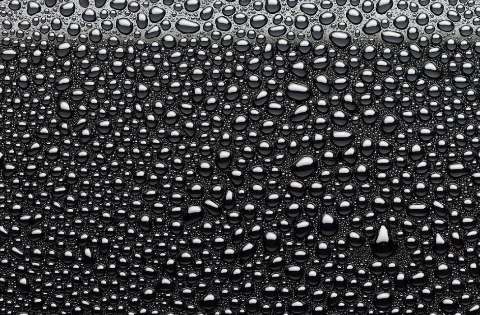 Close-up view of shiny water droplets covering a black surface, creating a captivating and textured abstract pattern.