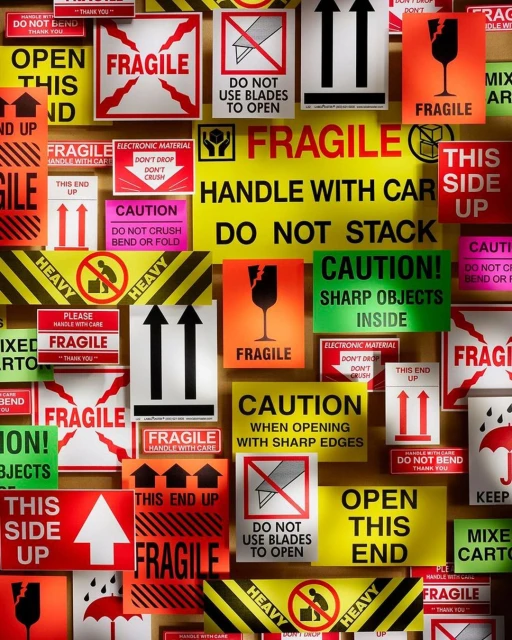 Collage of shipping and handling warning labels with 'Fragile,' 'Handle With Care,' 'Do Not Stack,' and 'This Side Up' directives on red, yellow, and white signs.