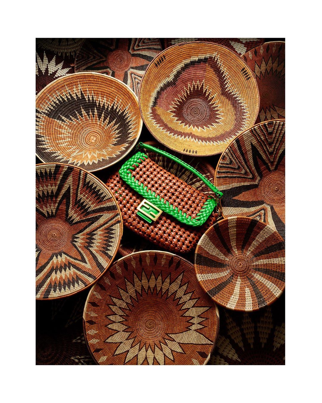 Close-up of woven brown handbag with green trim encircled by a collection of decorative woven baskets in neutral tones and geometric patterns.