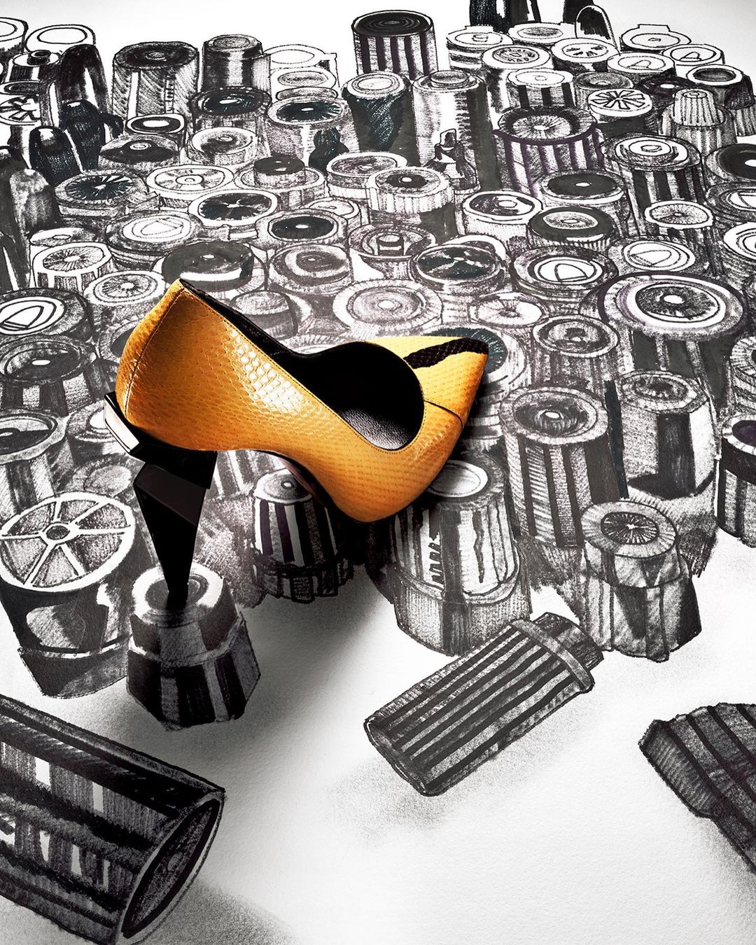 Fashion editorial shot: golden leather high heel pump shoe on a white surface surrounded by black and white cylinder drawings.