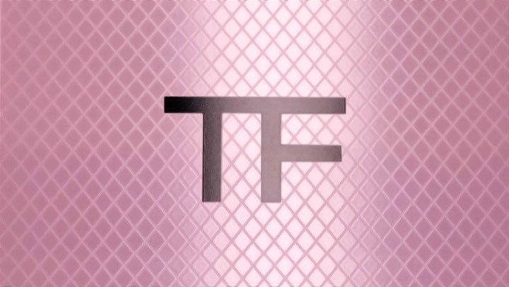 Close-up of silver TF logo on a pink diamond-patterned background. Minimalist fashion photography with soft, diffused lighting.