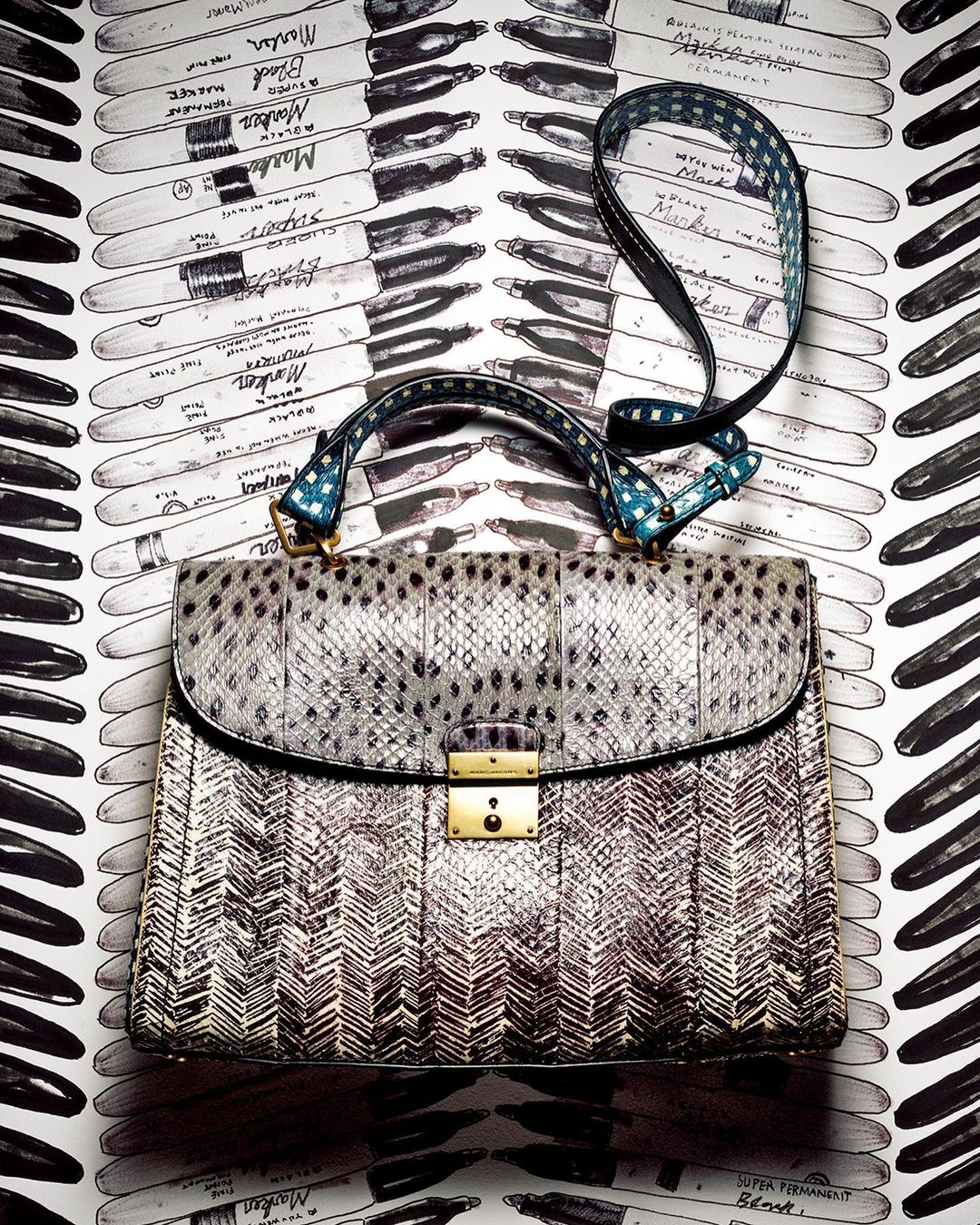 Fashionable handbag with snakeskin texture, gold clasp, and handle with polka dot accents against a marker-patterned backdrop.