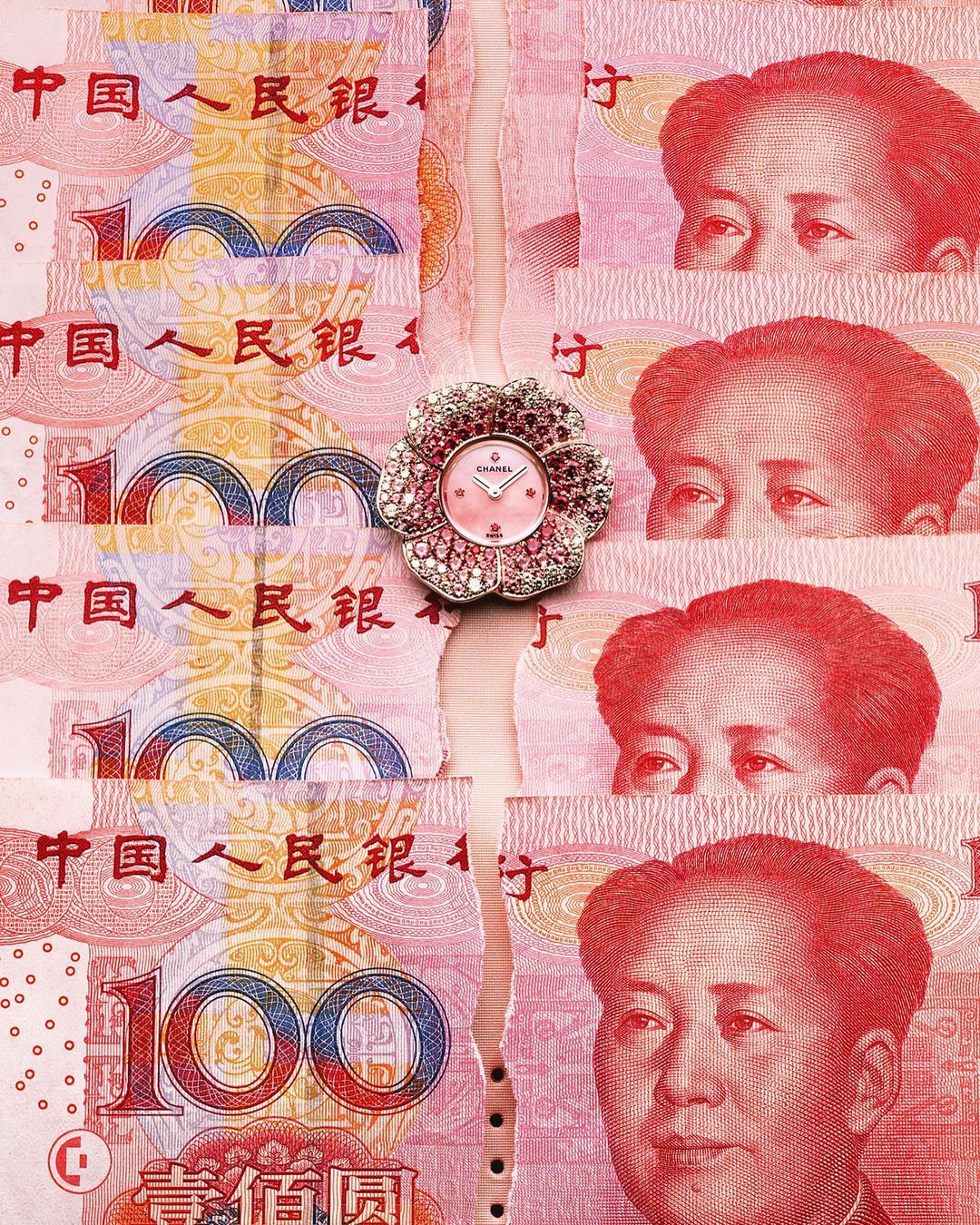 Close-up of a flower-shaped Chanel watch with a pink face, lying on top of shredded Chinese Yuan paper currency with Mao Zedong portraits.