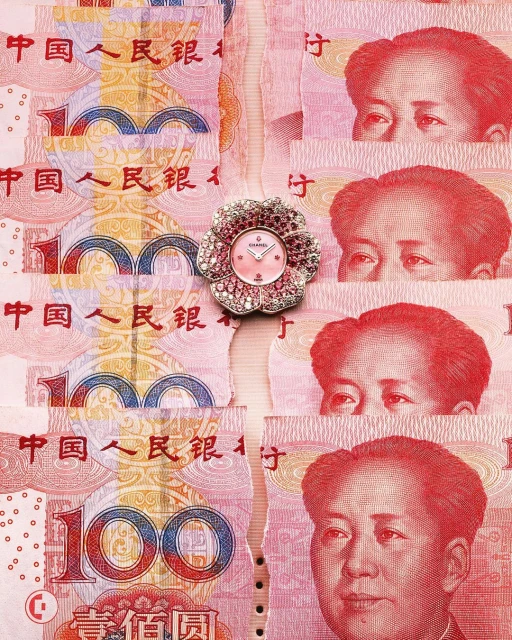 Close-up of a flower-shaped Chanel watch with a pink face, lying on top of shredded Chinese Yuan paper currency with Mao Zedong portraits.