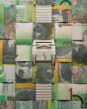 A creative still life features a diamond watch on a woven background of Australian one hundred dollar bills, highlighting luxury and finance.