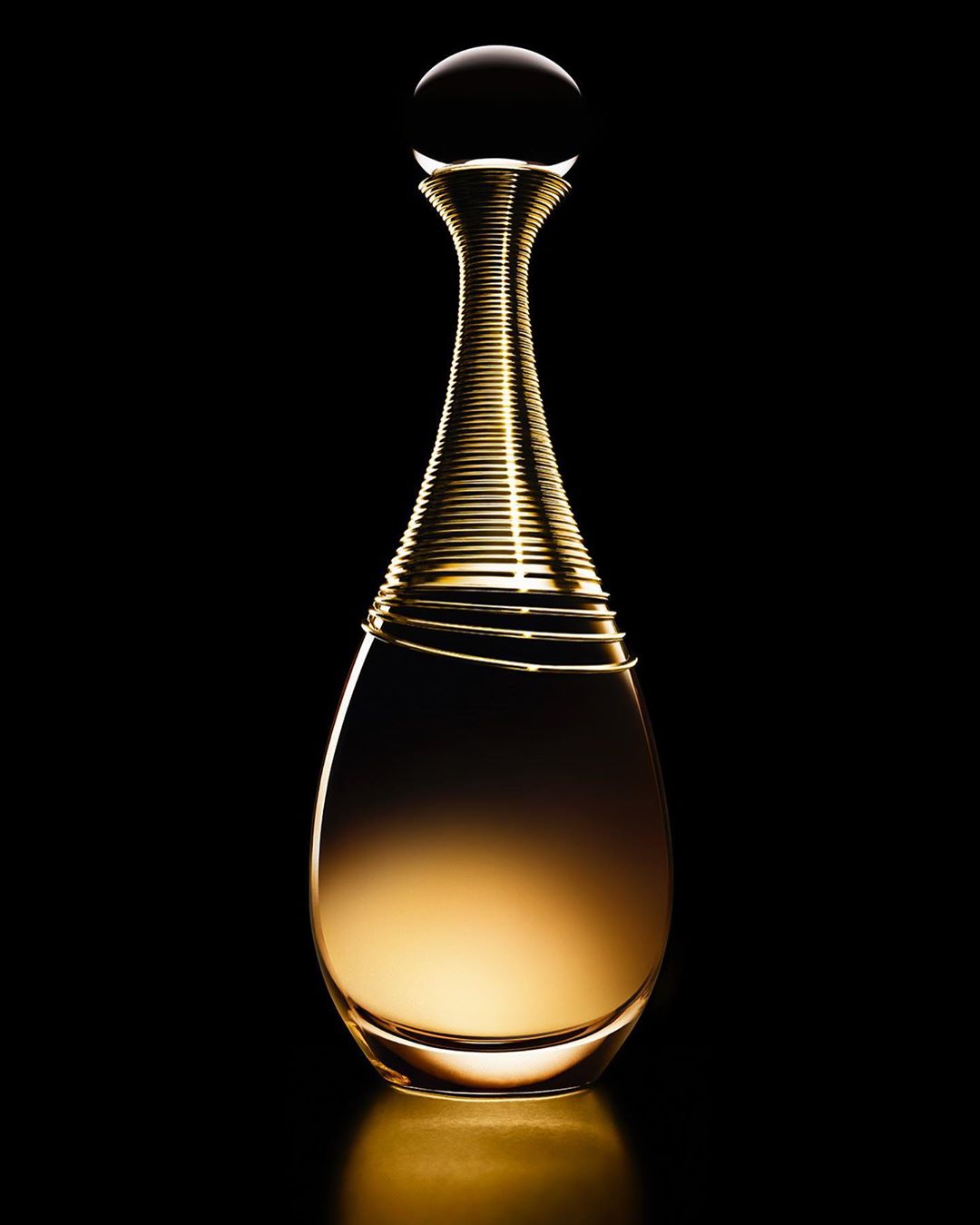 Close-up product photograph of a teardrop-shaped perfume bottle with a golden ribbed neck and spherical cap on a black background.
