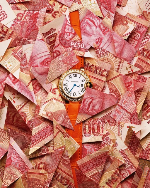 Wristwatch with a gold case and orange leather strap displayed atop a pile of cut-up Mexican currency, creating a visually striking composition.