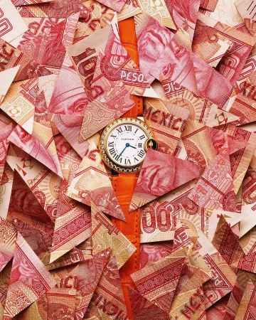 Wristwatch with a gold case and orange leather strap displayed atop a pile of cut-up Mexican currency, creating a visually striking composition.