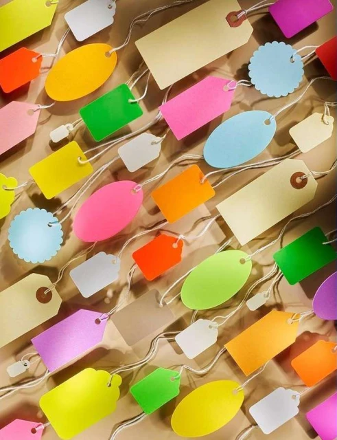 Multiple colourful tags of different shapes and sizes arranged on a light brown surface, connected with off-white strings.
