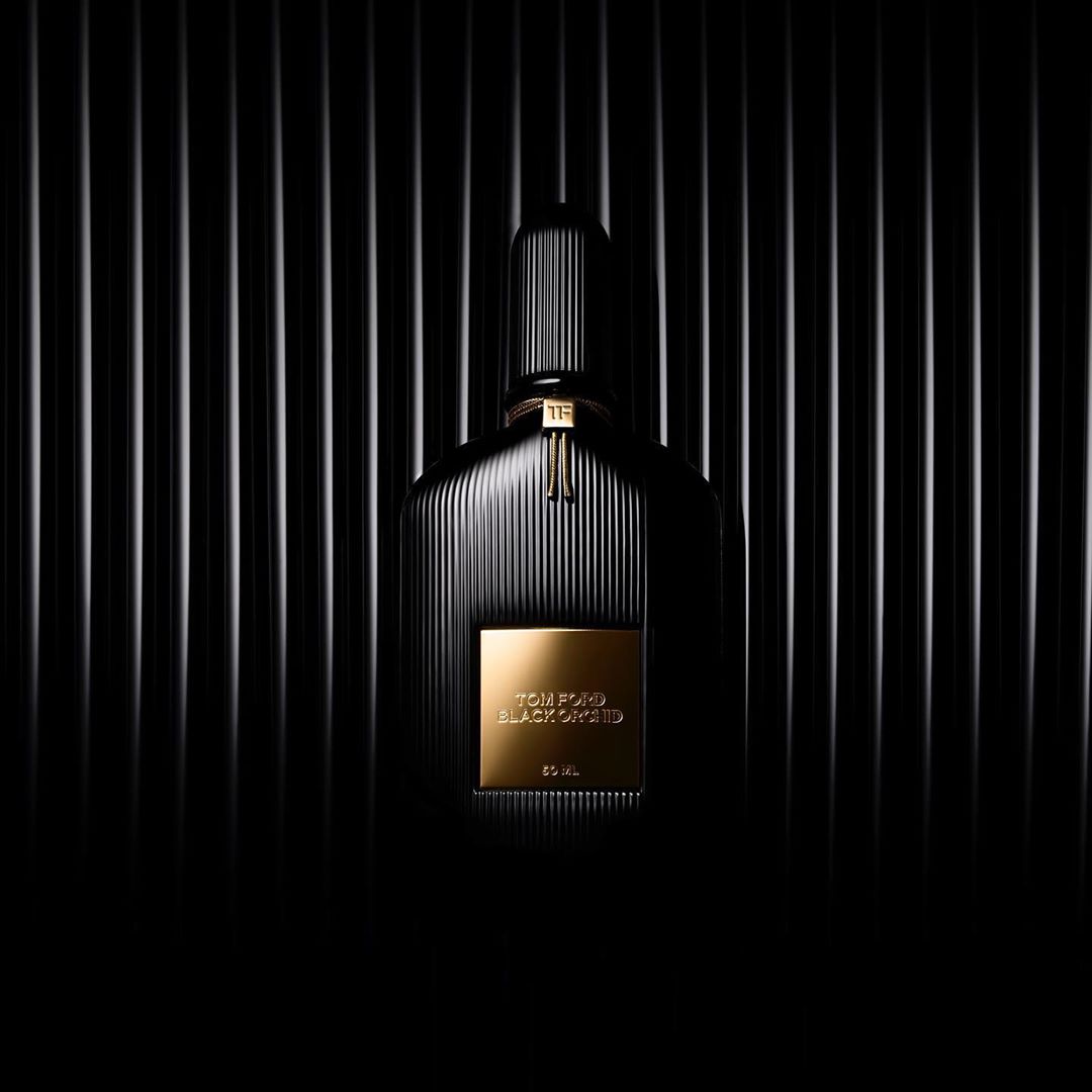 Black and gold Tom Ford Black Orchid perfume bottle against dark vertical striped background. Elegant product photography, beauty and cosmetics.