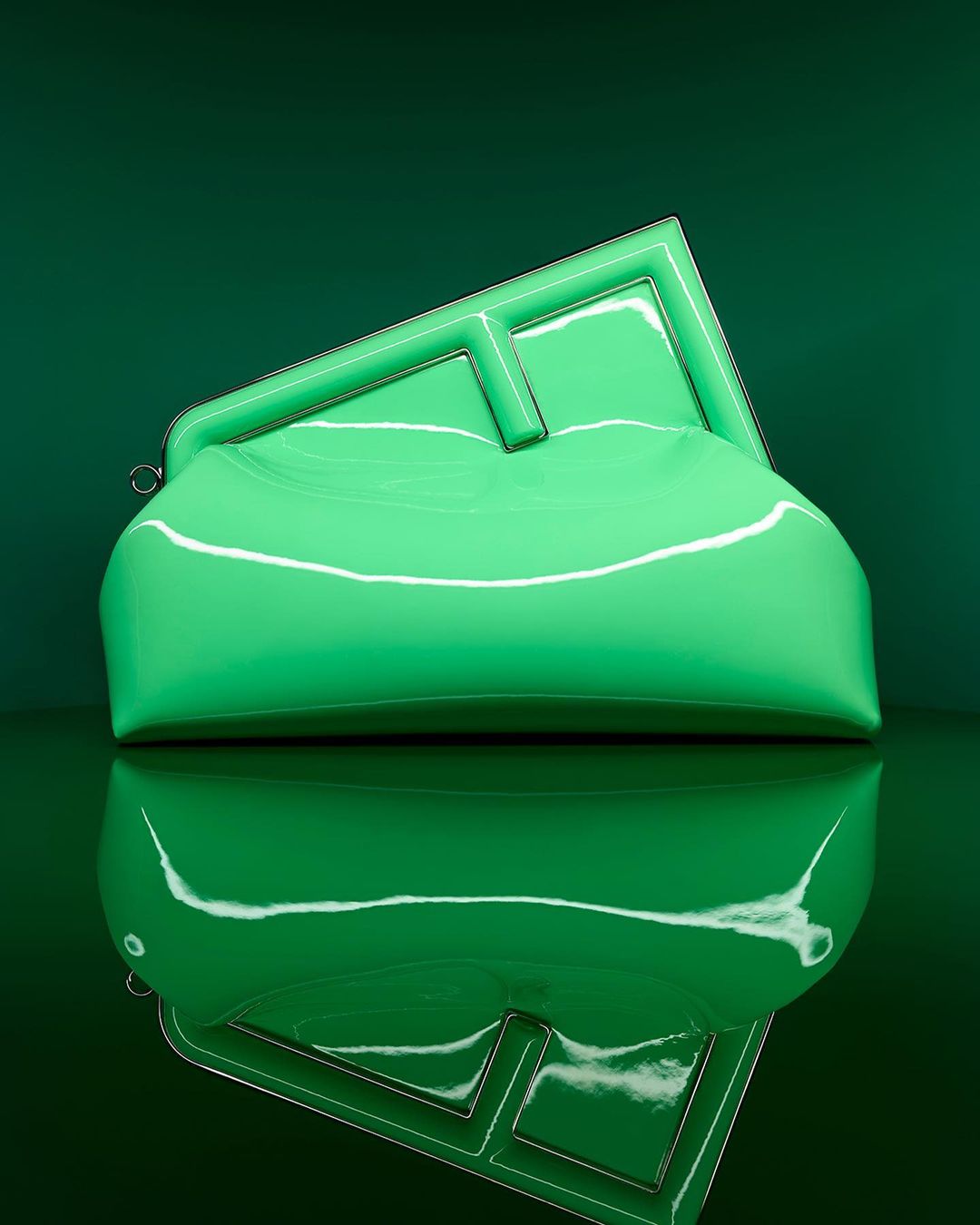 Stylish glossy green clutch purse with geometric frame and handle, reflecting against a glossy dark-green backdrop, studio lighting.