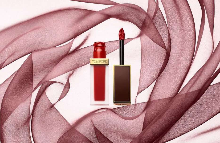 Tom Ford red matte lip lacquer displayed with product applicator on a light background with draped translucent fabric.