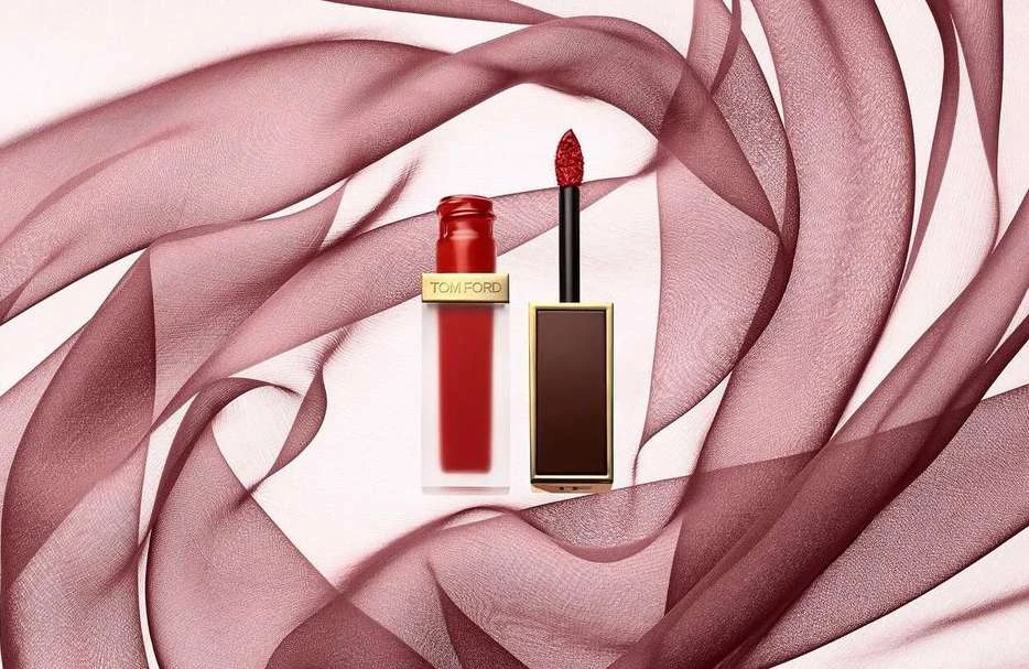 Tom Ford red matte lip lacquer displayed with product applicator on a light background with draped translucent fabric.