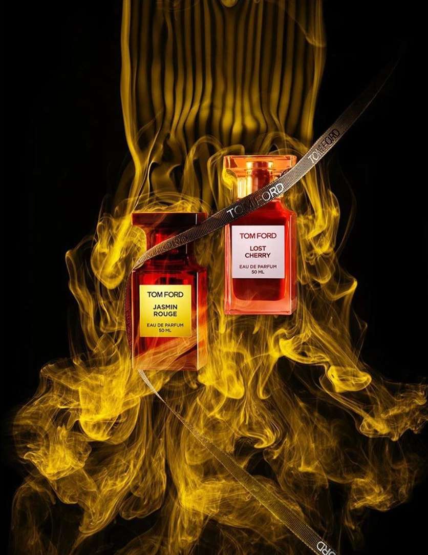 Tom Ford Jasmin Rouge and Lost Cherry perfume bottles with gold ribbon, presented against an abstract gold smoke background.