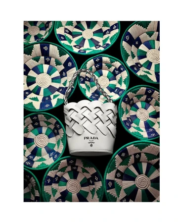 White leather Prada bucket bag centered against a dark background surrounded by patterned woven green bowls