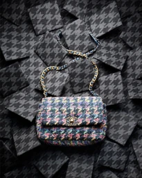 Multicolor tweed flap bag with chain strap centered on a background of dark grey houndstooth squares.