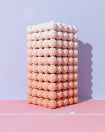 Stacked tennis balls create an unusual tower effect with color gradations in a whimsical studio shot against a pink and blue background.