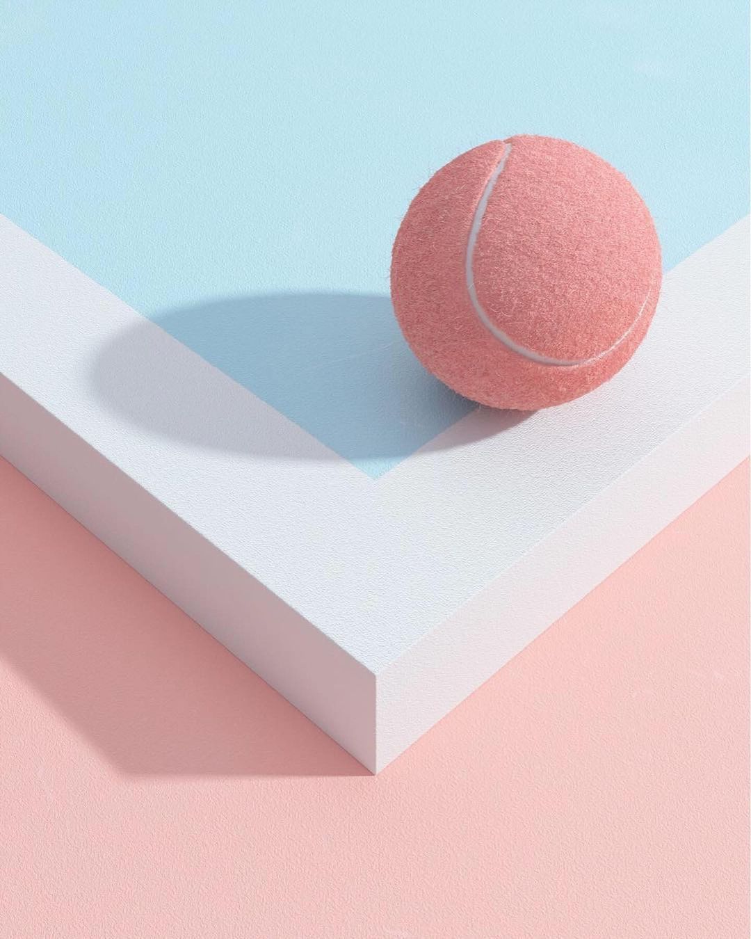 Pink tennis ball on a white surface against pastel pink and blue background, creating a minimalist and visually appealing composition.