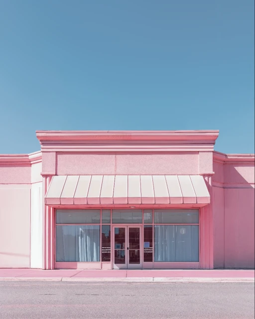 Pink-hued commercial building with a large glass storefront and light blue sky, creating a pastel aesthetic.