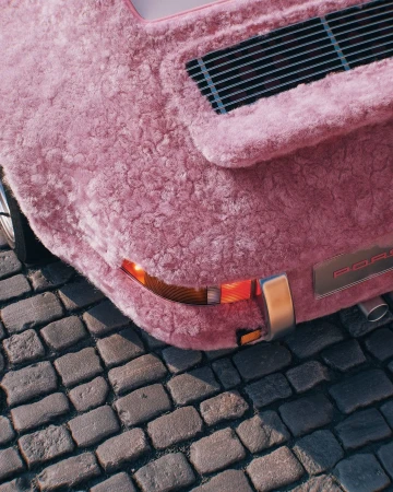 Close-up of a vintage pink Porsche covered in fur parked on a cobblestone street, showcasing its unique exterior and vintage style.