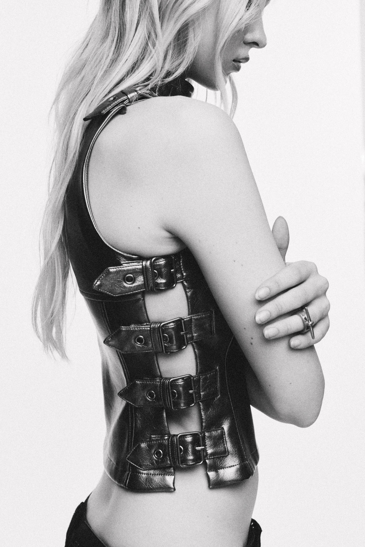 Black and white profile portrait of a woman wearing a black leather sleeveless top with buckled side straps against a white background.