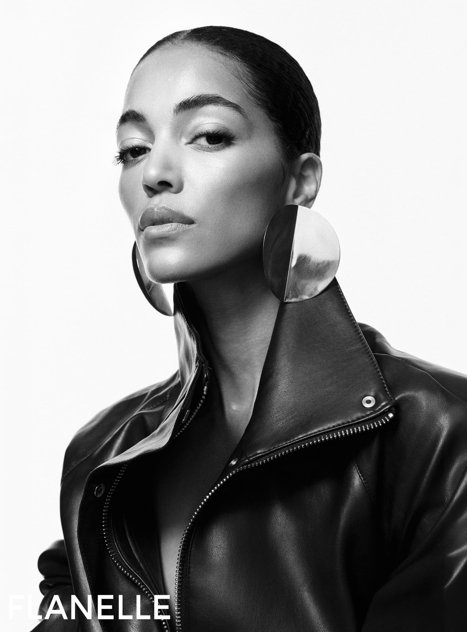 Model wearing large circular metallic earrings and a high-collar black leather jacket against a seamless white studio background.