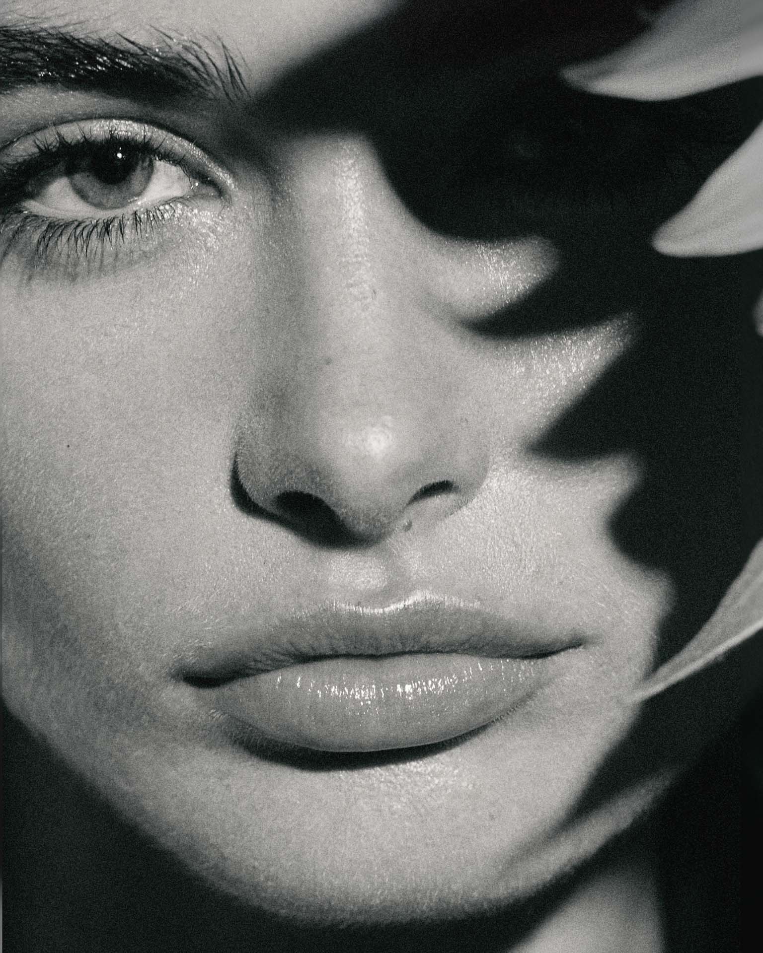 Extreme close-up portrait of a woman's face with dramatic shadow cast across her eyes by foliage, captured in monochrome.