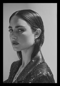 Black and white portrait of a woman with slicked-back dark hair, wearing a sequined jacket. She is indoors with a blurred background.