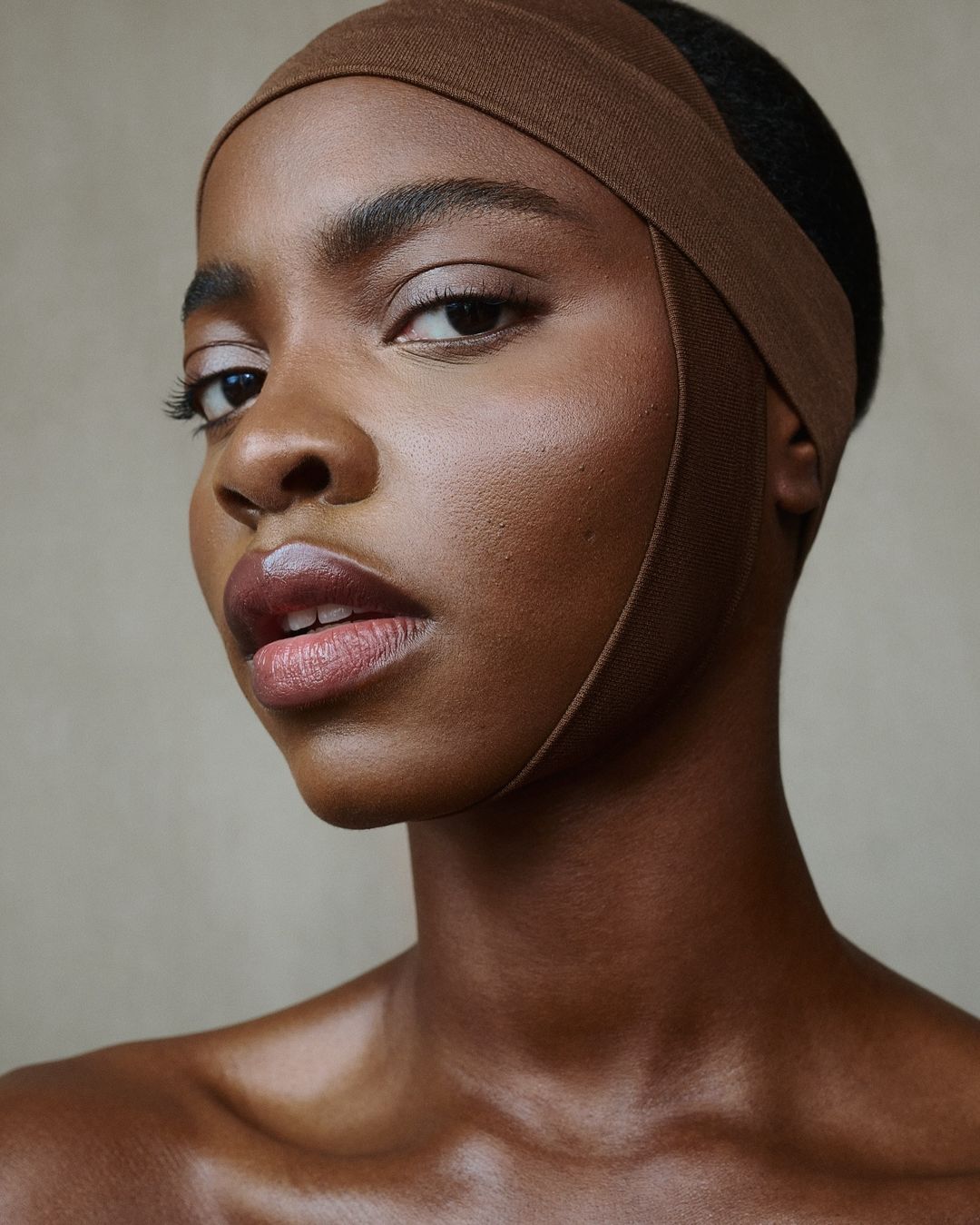 Close-up studio portrait of a Black woman with a brown headband, showcasing clean beauty and skincare. Neutral background and eye-level angle.