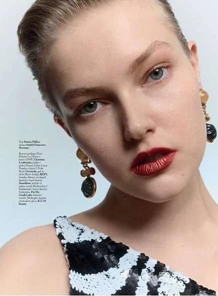 Close-up portrait of a fair-skinned adult woman with dark red lipstick, ornate earrings, and a black and white dress in a studio.
