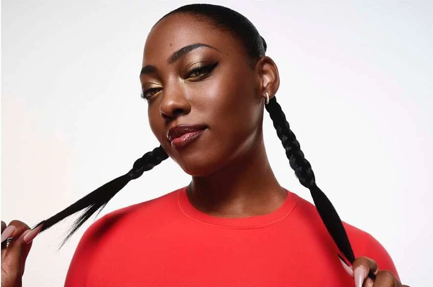 A dark-skinned woman poses with braided hair and red shirt against a white background, showcasing beauty and fashion elements.